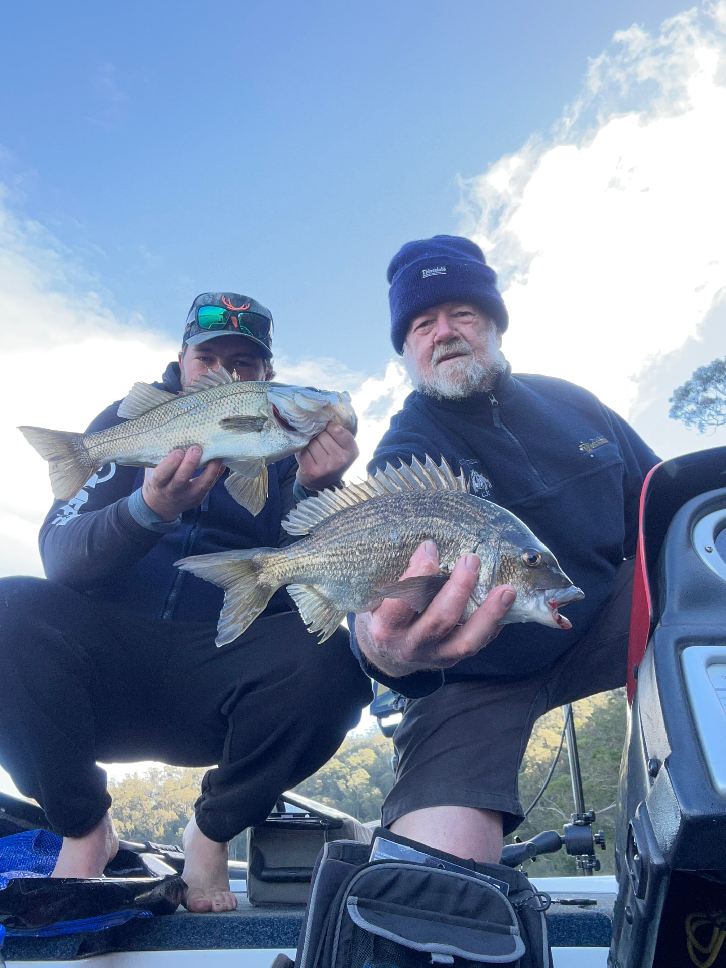 Two guests holding an estuary perch and a black bream caught on the lake