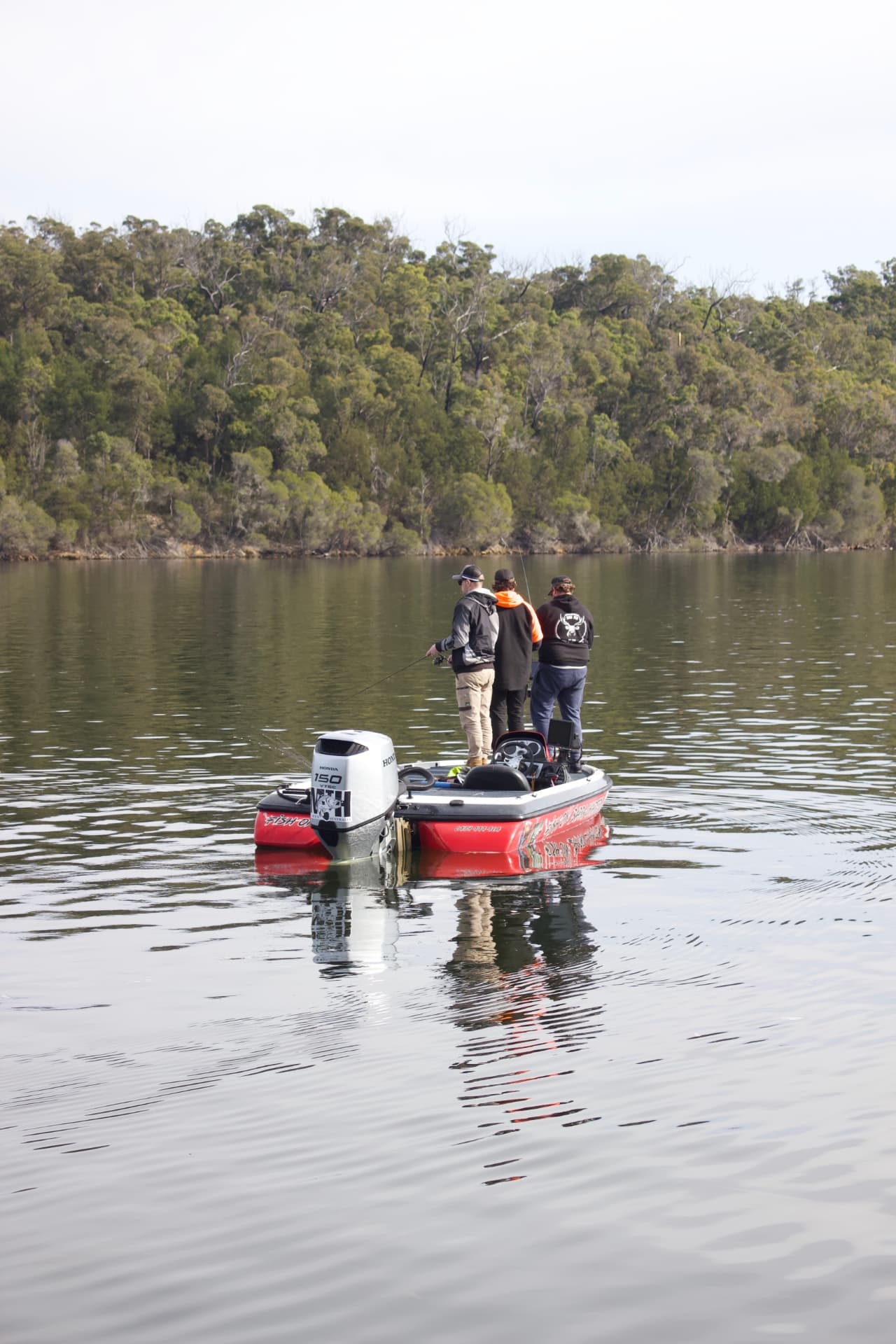 Three anglers casting from the boat against the forested lake shore